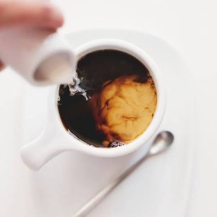 Cold milk being poured into a long black coffee